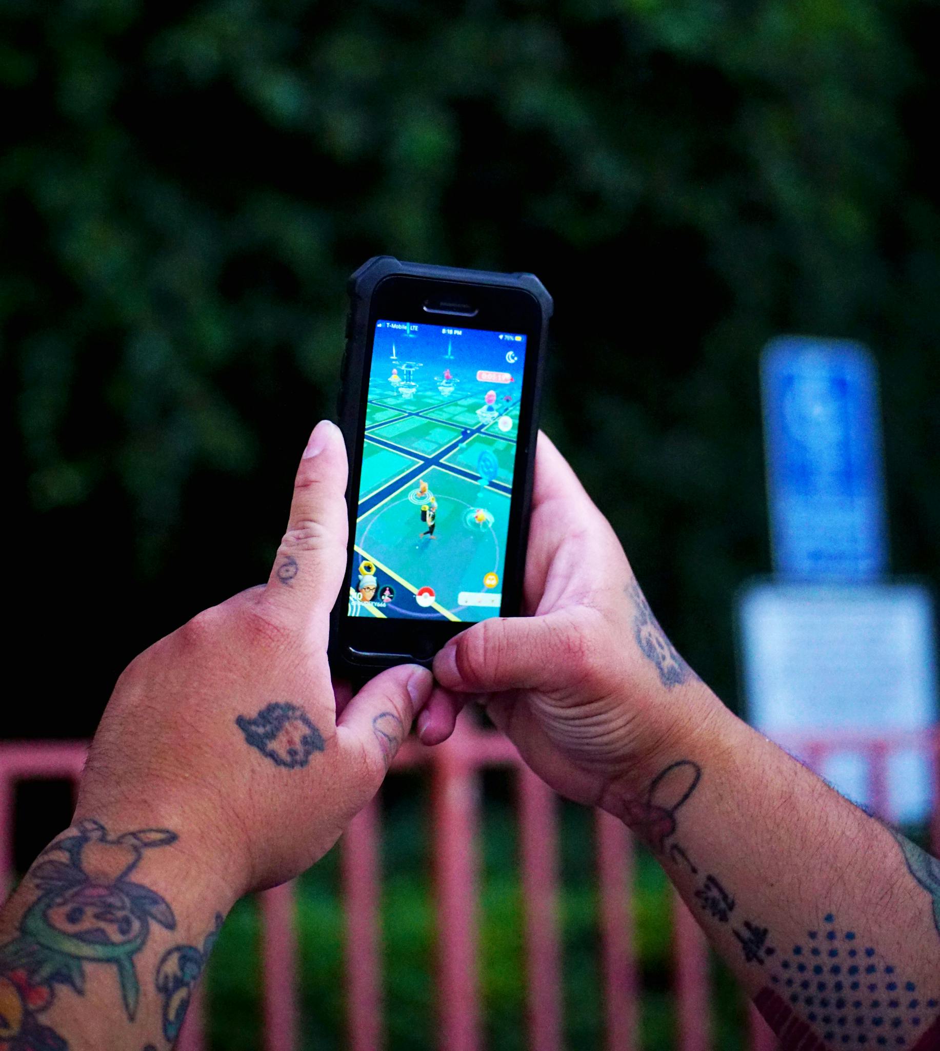 Close-up of hands with tattoos playing a mobile game outdoors on a smartphone.