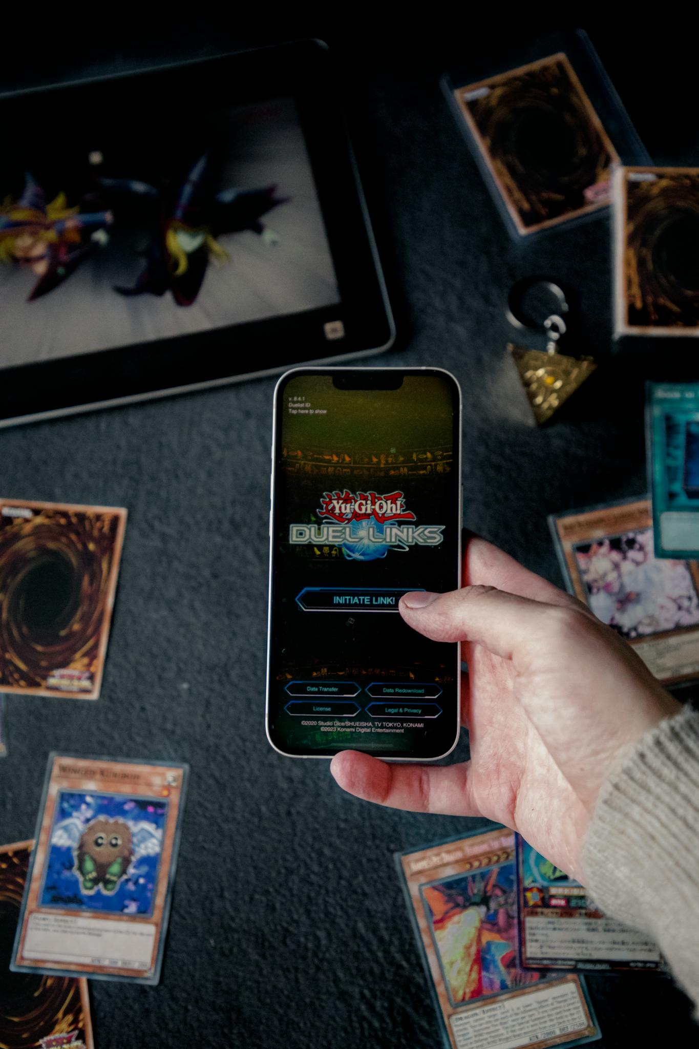 Yu-Gi-Oh! Duel Links app on a smartphone surrounded by trading cards.